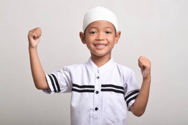 A happy and excited Muslim Asian boy with raised hands isolated on white background clipart