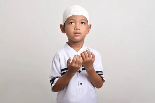 Asyalı Müslüman çocuk beyaz arka planda elleri açık dua ediyor. Tanrı 'ya içtenlikle dua ediyor, ellerini kaldırarak dua ediyor.