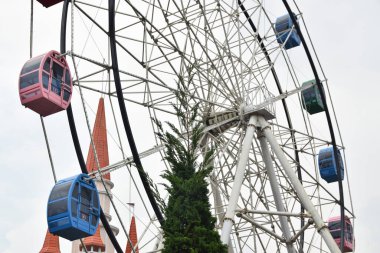 Bulutlu arka planda, lunaparkta renkli yolcu kabinleri olan dönme dolabın alt görüntüsü