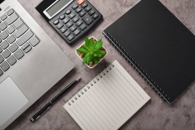 Muhasebe işyeri konsepti. Üst görünüm Hesaplayıcı, dizüstü bilgisayar, defter, kalem, gözlük ve bitkiler koyu gri masa üzerinde