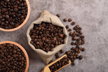 Ahşap kasede kavrulmuş kahve çekirdekleri ve koyu çimento arka planda izole edilmiş çuvallar. Üst görünüm