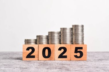 2025 yılına başlıyoruz. 2025 tahta küp blok ve para yığını. Teknoloji, vergi, finans, tasarruf kavramları