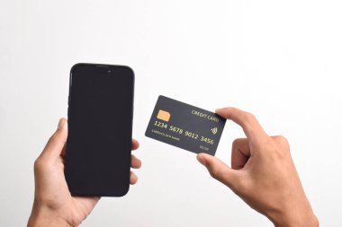 Cep telefonu tutan erkek eller ve beyaz arka planda izole edilmiş siyah kredi kartı. Mobil ödeme, çevrimiçi alışveriş kavramı