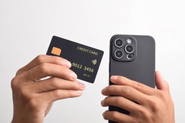 Cep telefonu tutan erkek eller ve beyaz arka planda izole edilmiş siyah kredi kartı. Mobil ödeme, çevrimiçi alışveriş kavramı