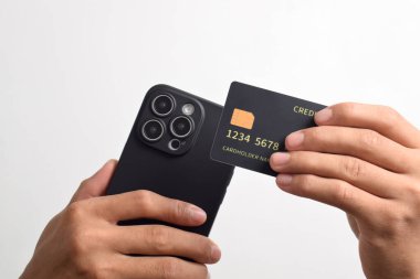 Cep telefonu tutan erkek eller ve beyaz arka planda izole edilmiş siyah kredi kartı. Mobil ödeme, çevrimiçi alışveriş kavramı