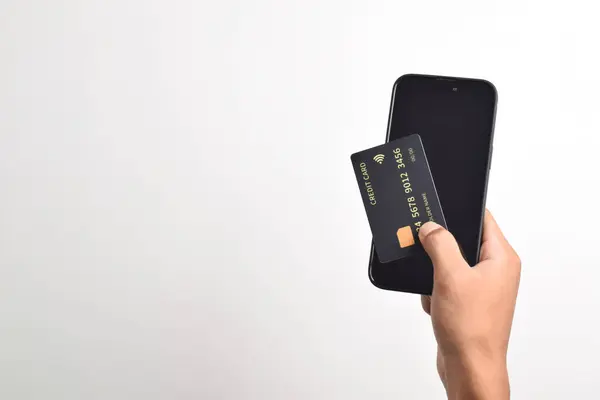 Cep telefonu tutan erkek eller ve beyaz arka planda izole edilmiş siyah kredi kartı. Mobil ödeme, çevrimiçi alışveriş kavramı
