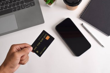 Ofis masasında el ele tutuşan kredi kartı, üst manzara. İnternet bankacılığı, ödeme, online alışveriş kavramı.
