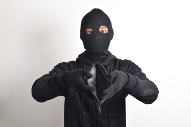 Siyah ceketli ve maskeli bir hırsız çalınan cüzdanını kontrol ediyor, beyaz arka planda izole edilmiş..