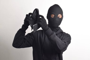 Siyah ceketli ve maskeli bir hırsız çalınan cüzdanını kontrol ediyor, beyaz arka planda izole edilmiş..