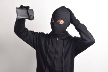 Siyah ceketli ve maskeli bir hırsız çalınan cüzdanını kontrol ediyor, beyaz arka planda izole edilmiş..