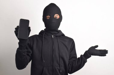 Siyah kapüşonlu ve maskeli gizemli bir adam akıllı telefondan bilgisayar korsanlığı yapıyor, kafası karışmış, beyaz arka planda izole edilmiş..