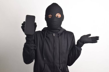 Siyah kapüşonlu ve maskeli gizemli bir adam akıllı telefondan bilgisayar korsanlığı yapıyor, kafası karışmış, beyaz arka planda izole edilmiş..