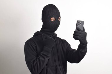 Siyah kapüşonlu ve maskeli gizemli adam akıllı telefondan hackleme faaliyetinde başarılı ve mutlu bir ifadeyle beyaz arka planda izole edilmiş..