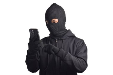 Siyah kapüşonlu ve maskeli gizemli bir adam cep telefonunda hackerlık yapıyor, akıllı telefon tutuyor, beyaz arka planda izole edilmiş..