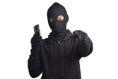 Siyah kapüşonlu ve maskeli gizemli adam akıllı telefondan hackleme faaliyetleri yapıyor, kamerayı işaret ediyor, beyaz arka planda izole edilmiş..