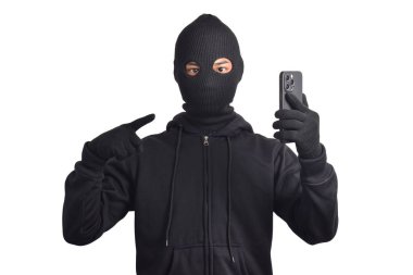 Siyah kapüşonlu ve maskeli gizemli adam akıllı telefondan hackleme aktivitesi yapıyor, akıllı telefonu işaret ediyor, beyaz arka planda izole edilmiş..