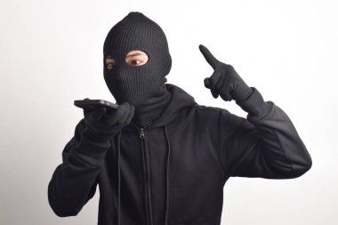Siyah kapüşonlu ve maskeli gizemli bir adam. Akıllı telefondan para sızdırıyor, beyaz arka planda izole edilmiş..