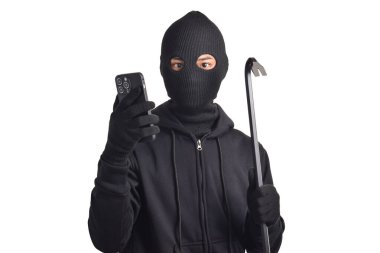 Siyah kapüşonlu ve maskeli gizemli adam cep telefonunda hackerlık yapıyor, akıllı telefon ve levye tutuyor, beyaz arka planda izole edilmiş..