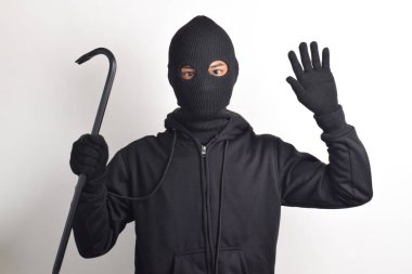 Siyah ceketli ve maskeli bir hırsız levye tutuyor, elleri havada teslim oluyor, beyaz arka planda izole edilmiş..