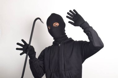 Siyah ceketli ve maskeli bir hırsız levye tutuyor, elleri havada teslim oluyor, beyaz arka planda izole edilmiş..