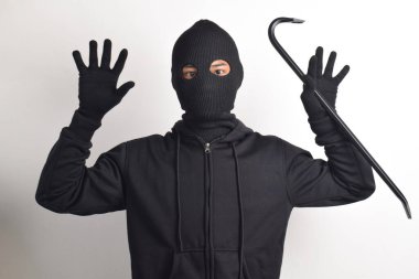 Siyah ceketli ve maskeli bir hırsız levye tutuyor, elleri havada teslim oluyor, beyaz arka planda izole edilmiş..