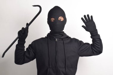 Siyah ceketli ve maskeli bir hırsız levye tutuyor, elleri havada teslim oluyor, beyaz arka planda izole edilmiş..