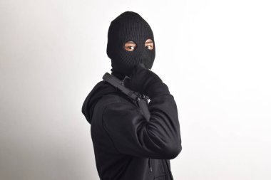 Siyah kapüşonlu ve maskeli silahlı gizemli bir adam, beyaz arka planda izole edilmiş..