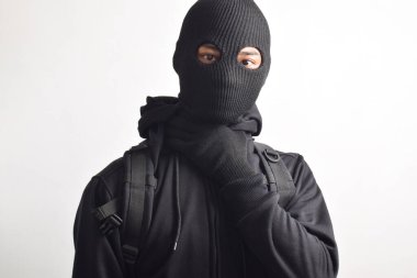 Beyaz arka planda siyah ceket, sırt çantası ve maske giyen bir hırsız var. Soygun ve suç kavramı