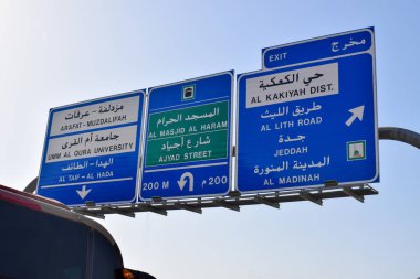 Mekke 'deki yol işaretleri, açık mavi gökyüzü altında Mescid-i Haram, Arafat, Medine ve Jeddah' a giden yolları gösteriyor..