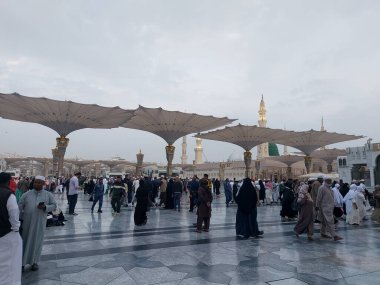 Al-Madinah al-Munawwarah, Suudi Arabistan - 27 Şubat 2025: Medine 'de Peygamberin Camii açık şemsiyeler ve minarelerle bulutlu bir gökyüzü altında, İslami mimariyi gözler önüne seren.