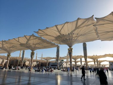 Al-Madinah al-Munawwarah, Suudi Arabistan - 1 Mart 2025: Açık mavi gökyüzü altında açık şemsiyeler ve minarelerle Medine 'deki Peygamber Camii.