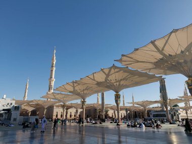 Al-Madinah al-Munawwarah, Suudi Arabistan - 1 Mart 2025: Açık mavi gökyüzü altında açık şemsiyeler ve minarelerle Medine 'deki Peygamber Camii.