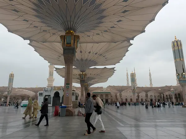 Al-Madinah al-Munawwarah, Suudi Arabistan - 27 Şubat 2025: Medine 'de Peygamberin Camii açık şemsiyeler ve minarelerle bulutlu bir gökyüzü altında, İslami mimariyi gözler önüne seren.