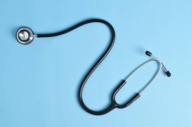 Açık mavi arka planda siyah steteskop izole edilmiş. düz yatış, üst görünüm
