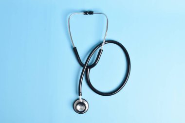 Açık mavi arka planda siyah steteskop izole edilmiş. düz yatış, üst görünüm