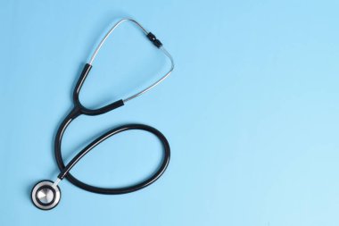 Stetoskop açık mavi arka planda, üst görüntüde izole edilmiş. Tıbbi araç