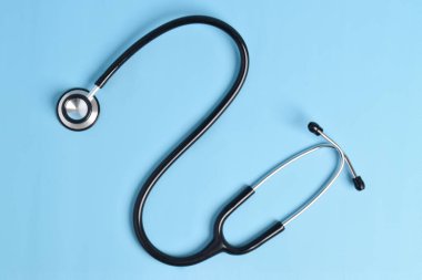 Açık mavi arka planda siyah steteskop izole edilmiş. düz yatış, üst görünüm