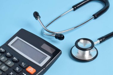 Açık mavi arkaplanda stetoskop ve hesap makinesi, yakın plan