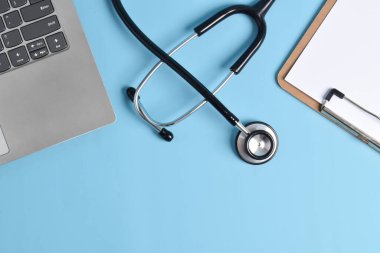 Laptop, steteskop ve açık mavi masadaki boş pano, üst manzara. Doktorun işyeri