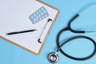 Stetoskop, boş pano ve açık mavi arka planda ilaçlar. Kardiyoloji ve sağlık konsepti.