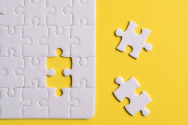 Sarı arka planda eksik parçalı beyaz bulmaca. Düz yatıyordu. Üst görünüm