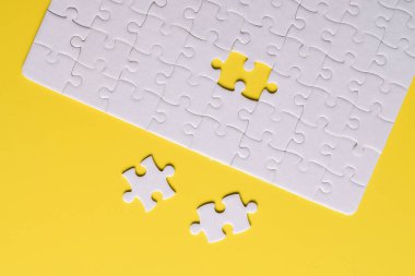 Sarı arka planda eksik parçalı beyaz bulmaca. Düz yatıyordu. Üst görünüm