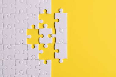 Sarı arka planda eksik parçalı beyaz bulmaca. Düz yatıyordu. Üst görünüm