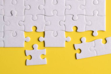 Sarı arka planda eksik parçalı beyaz bulmaca. Düz yatıyordu. Üst görünüm