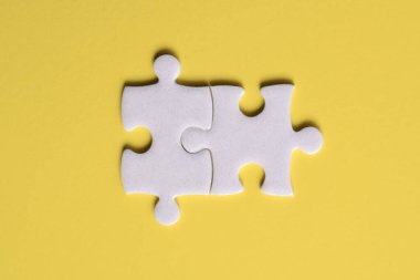 Sarı arka planda iki beyaz yapboz parçası. Üst görünüm