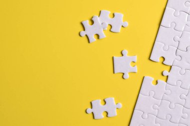 Sarı arka planda eksik parçalı beyaz bulmaca. Düz yatıyordu. Üst görünüm