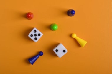 Renkli masa oyunu figürleri ve turuncu arkaplanda izole edilmiş zarlar