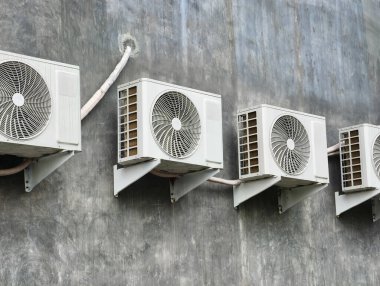 Birçok açık hava havalandırma ünitesi gri, desenli beton bir duvarda bir sırada monte edilir..