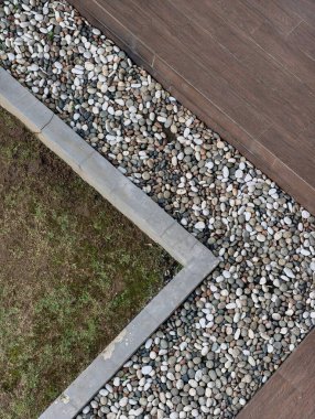 Close-up view of a garden border featuring small stones, concrete edging, and a wooden deck.