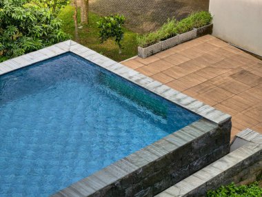 A tranquil swimming pool surrounded by vibrant plants and a warm wooden deck, perfect for relaxation.